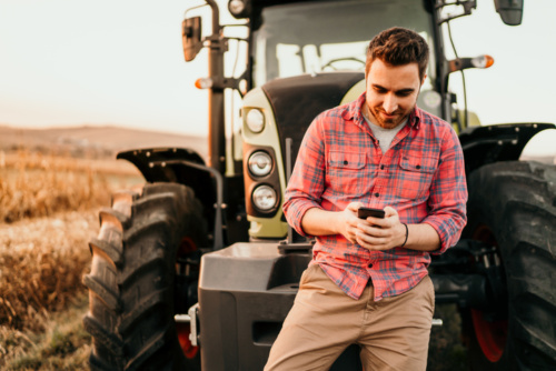 Portrait of smiling farmer using smartphone and tractor at harvesting.